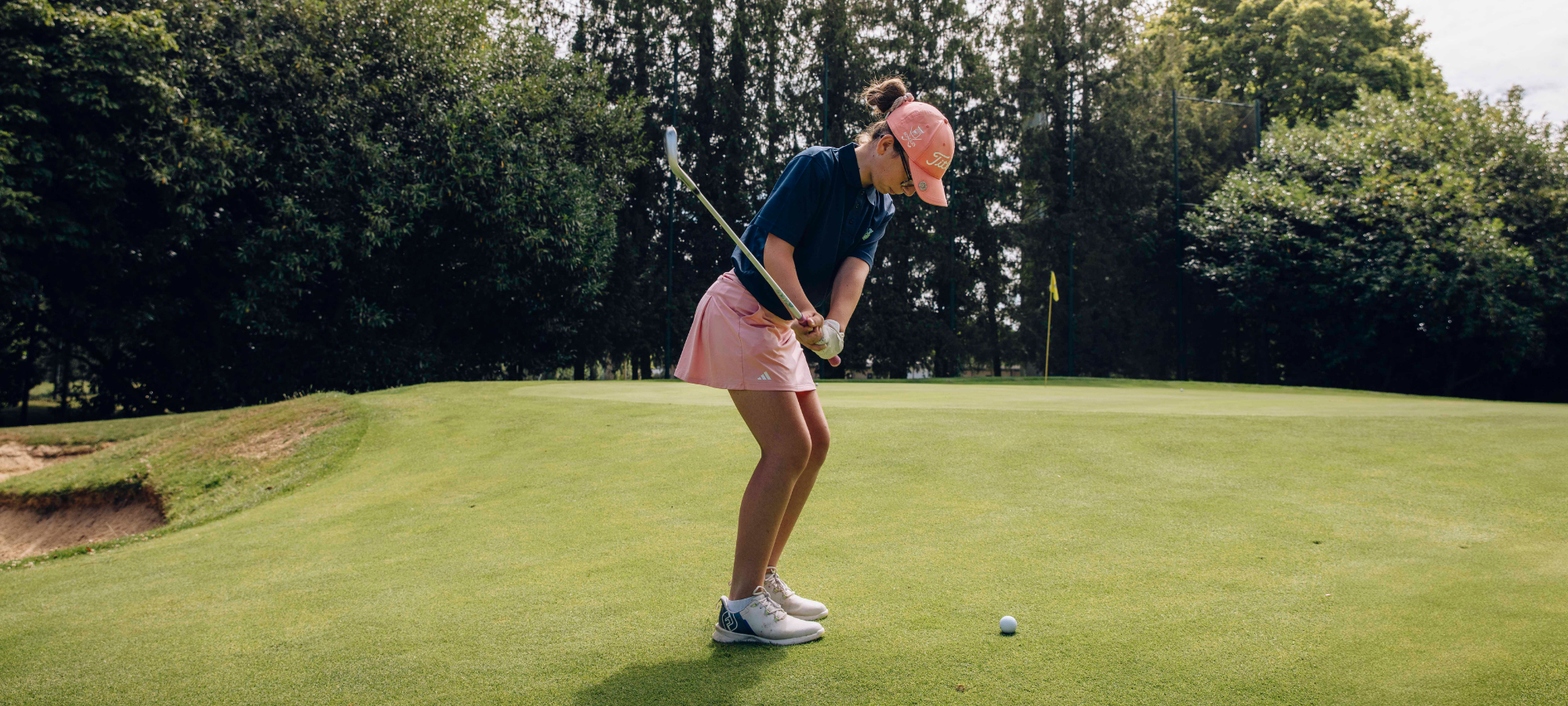 Jeune golfeur en polo s'apprêtant à frapper la balle sur un parcours au printemps.