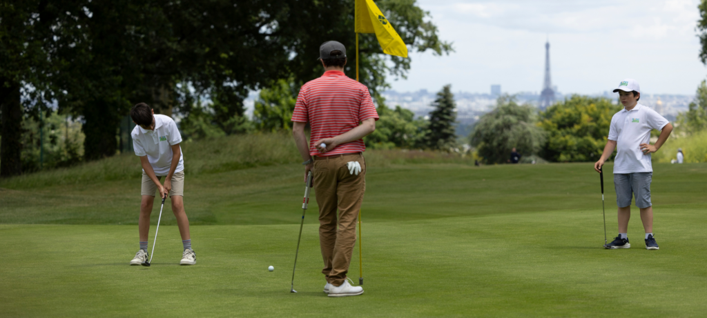 Jeune golfeur de 8 à 14 ans concentré sur son putting pendant qu'un parent l'encourage au bord du green.