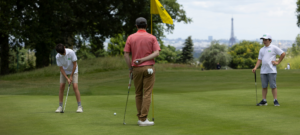 Jeune golfeur de 8 à 14 ans concentré sur son putting pendant qu'un parent l'encourage au bord du green.