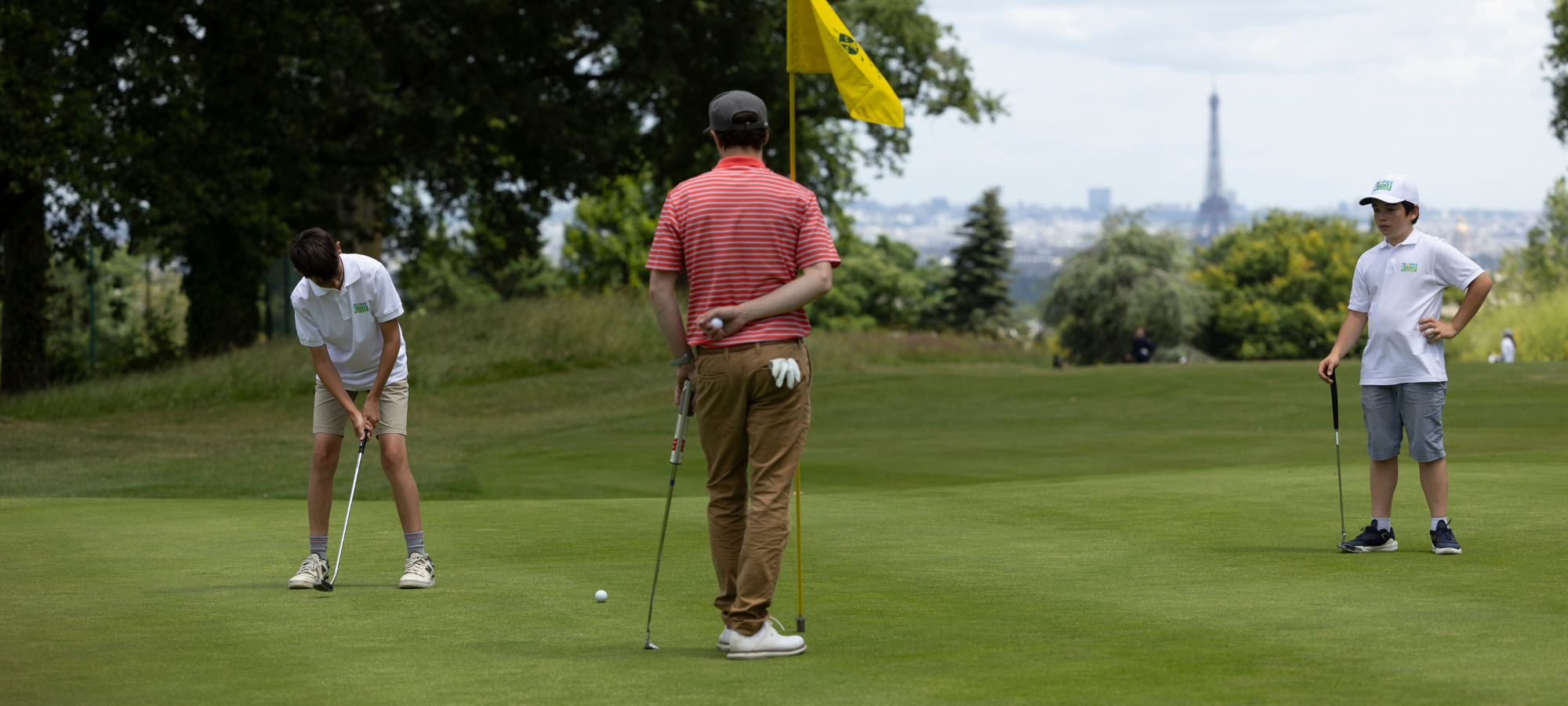 Jeune golfeur de 8 à 14 ans concentré sur son putting pendant qu'un parent l'encourage au bord du green.
